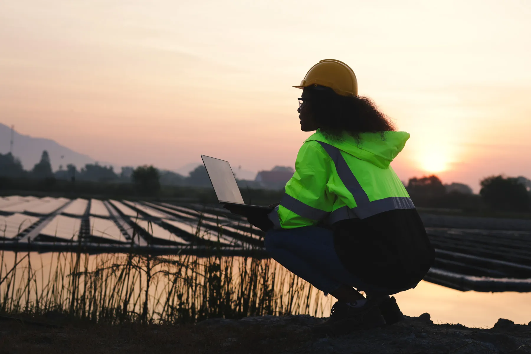 Black solar engineer with green safety jacket and laptop working at Solar floating site
